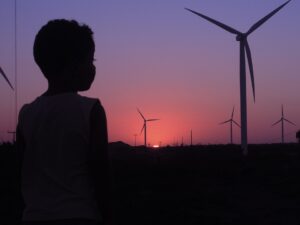 Un bambino guarda pale eoliche al tramonto. Foto di copertina di un articolo pubblicato su secondo welfare in cui Paola Gilardoni di Cisl riflette sulle opportunità occupazionali della transizione energetica in Lombardia