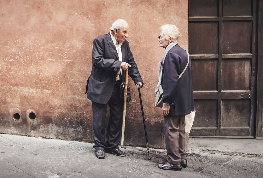 Due anziani, un uomo o una donna, discutono su una strada leggermente in salita. Immagine di copertina di un articolo di Secondo Welfare firmato da Franca Maino e Valeria De Tommaso che approfondisce i contenuti della legge delega sulla non autosufficienza approvato dal parlamento il 21 marzo