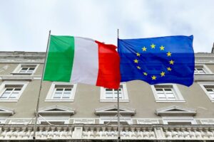 Bandiere italiane e europea davanti a un palazzo pubblico. Immagine di copertina dell'articolo di Percorsi di secondo welfare "Pubblica Amministrazione: è il momento del welfare aziendale"